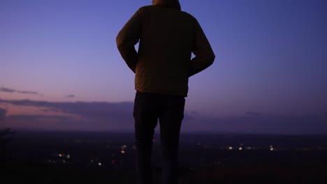 man in yellow jacket looks out to purple sunset