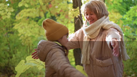 mother throws autumn leaves in air with joy as daughter twirls then hugs her lovingly under warm golden forest light, sharing emotional connection and playful happiness during peaceful fall moment