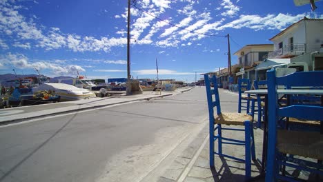 charming coastal street in santorini, greece with vibrant blue chairs and clear skies. sunlit harbor with anchored boats creates a serene and inviting atmosphere, perfect for a leisurely stroll.