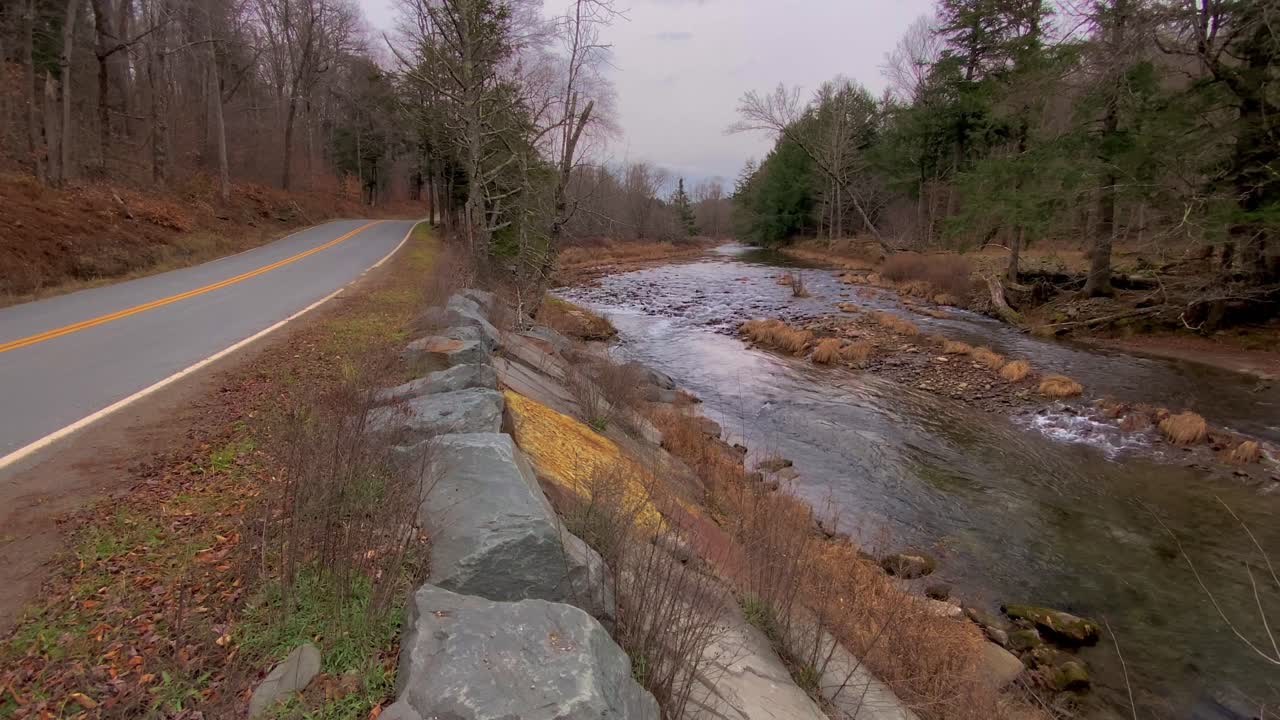 un arroyo que corre a lo largo de una carretera de montaña en un triste día de principios de invierno