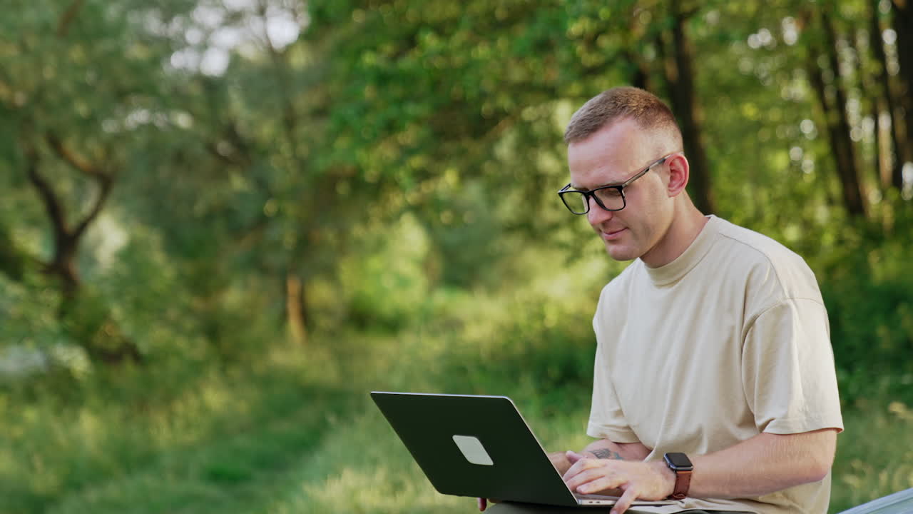 Busy man working in the natural surroundings. Freelancer looks at laptop sitting on the car.