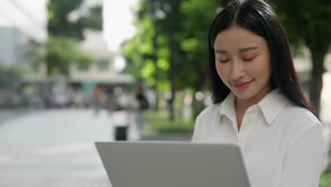 young asian woman using a laptop outdoors in an urban environment