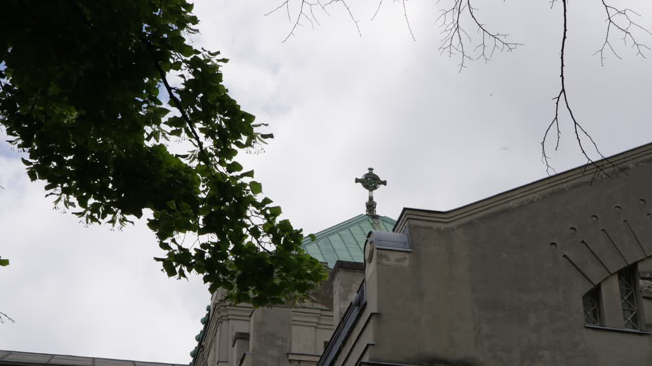 Edificio del cimitero Zentralfriedhof e un tiglio a Vienna, Austria. Architettura storica neobarocca con tetto in rame patinato e guglia a croce sotto un cielo coperto.
