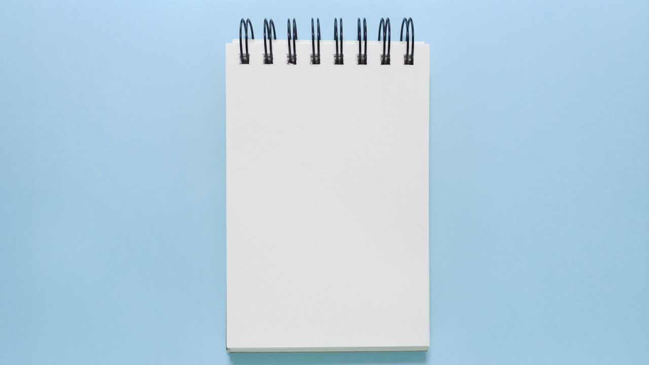 Stop motion of a blank spiral sketchbook sliding onto a blue backdrop, ideal for copy space
