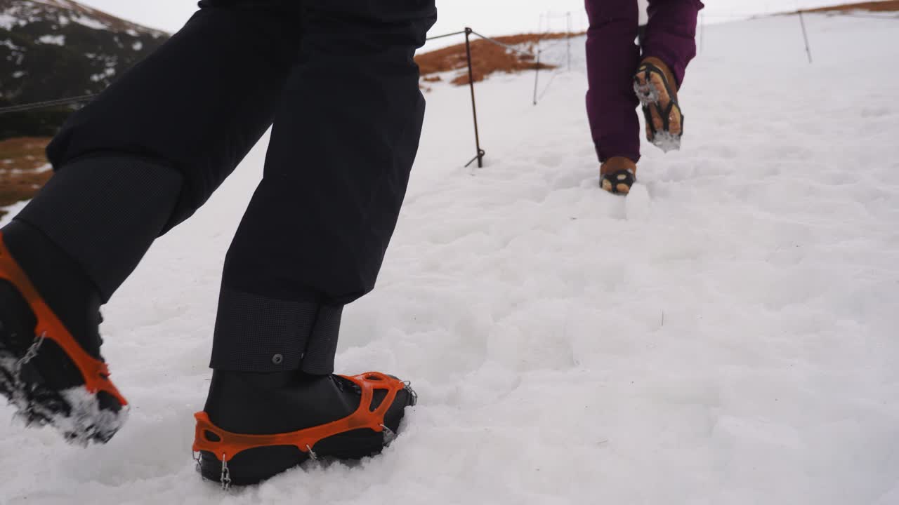 una pareja caminando por un sendero cuesta arriba en nieve helada con crampones en sus zapatos