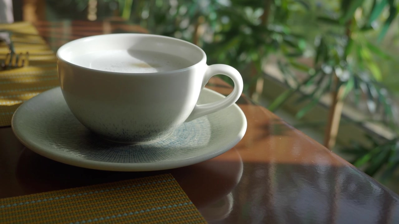 Tazza di caffè bianca con schiuma su un tavolo in un caffè soleggiato.