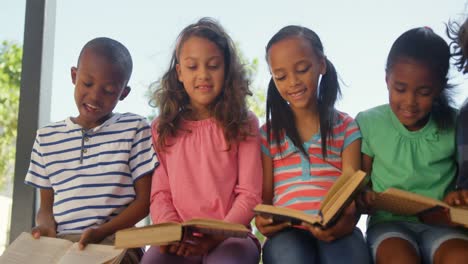 vista frontal de escolares de raza mixta leyendo libros en el corredor 4k