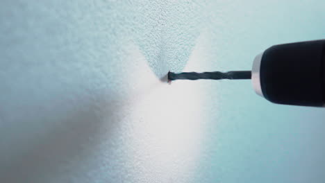 young male handyman using power drill with light to drill a hole in a white wall at home detail close up 4k