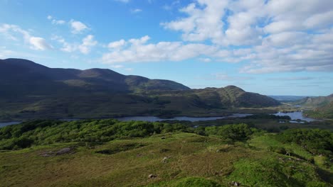 drone flying above a traveler woman rising arm in front of green landscape with lakes