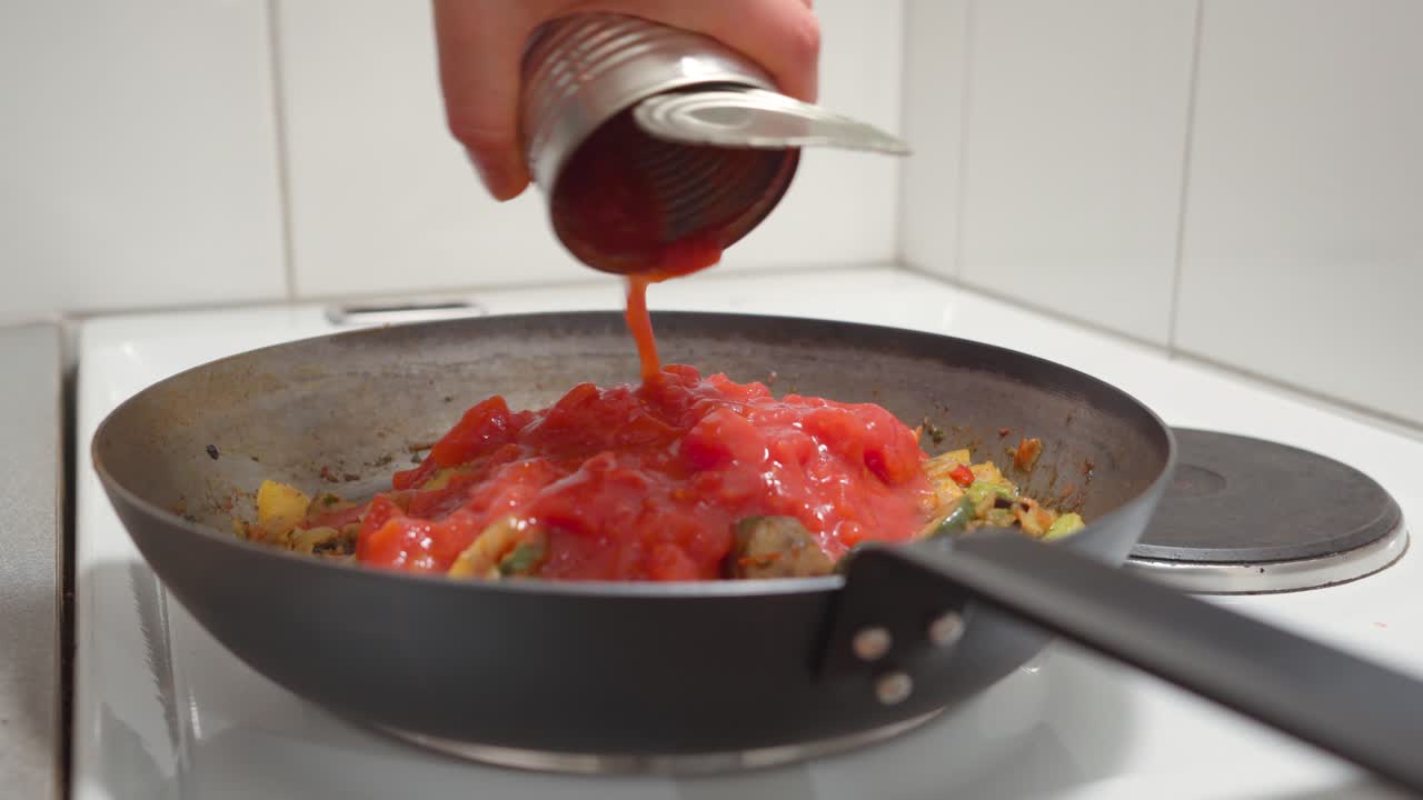 hombre vertiendo tomates triturados en verduras fritas en una sartén