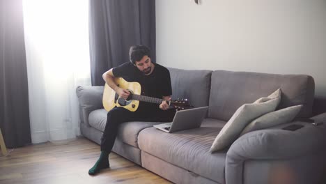 a young man plays the guitar through a video call on a laptop or practicing at home