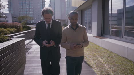 focused managers walking and using smartphones in city