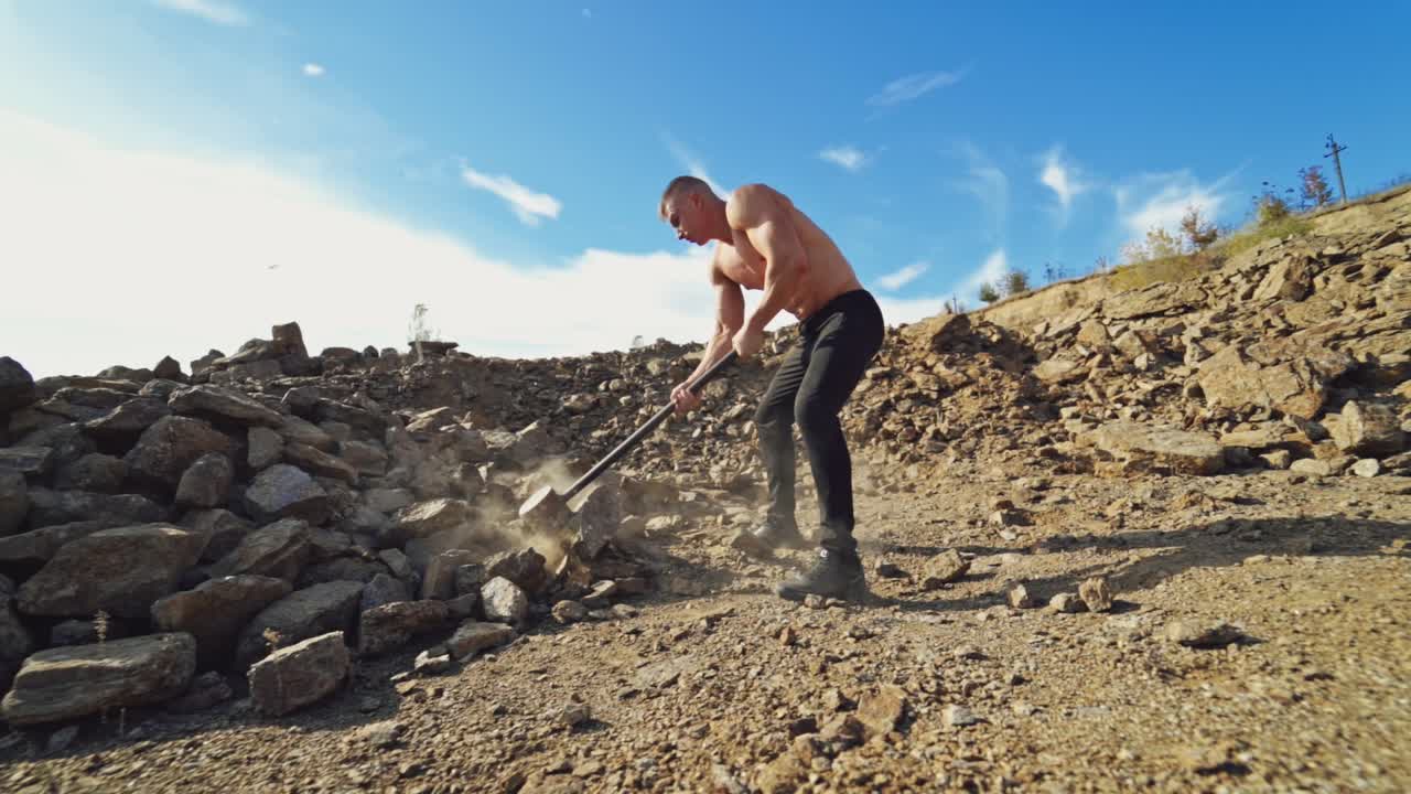 Shirtless sportsman with huge hammer outdoors. Strong athlete breaking stones with a hard steel hammer on the rocky hill background.
