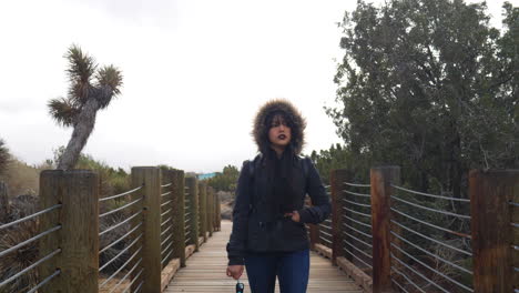 a pretty woman looking sad and moody as she walks a bridge in the desert under a cloudy, stormy sky slow motion
