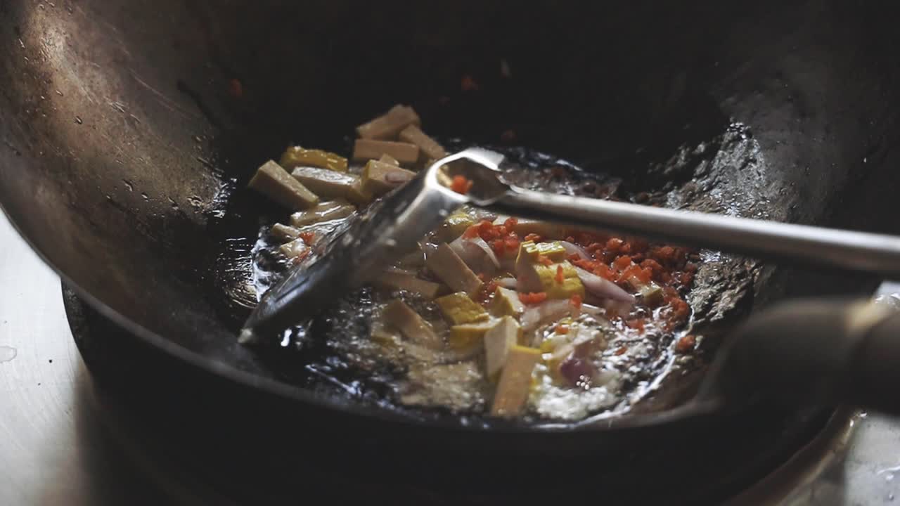 Cooking Pad Thai Series: SLO MO chef throwing in small dried shrimps and stir-frying shrimps and tofu in hot pan at Thai street food restaurant.