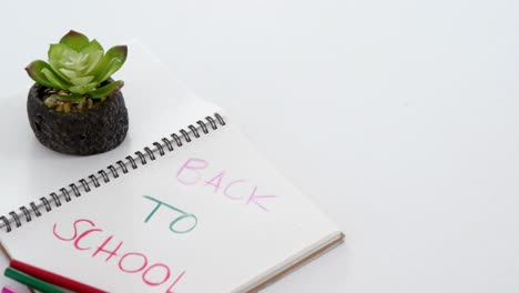 back to school text on open diary with colored pencils and sapling plant