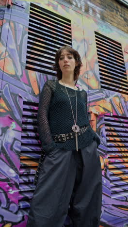 Vertical-Video-Outdoor-Fashion-Portrait-Of-Young-Alternative-Style-Woman-Leaning-Against-Graffitti-Covered-Wall-In-London-City-Street-UK-In-Real-Time-1