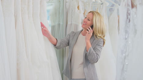 Mature-Female-Owner-Of-Bridal-Wedding-Dress-Shop-Talking-On-Mobile-Phone