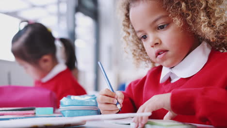 Cerca-De-Una-Colegiala-De-Raza-Mixta-Sentada-En-Un-Escritorio-En-Un-Aula-De-Escuela-Infantil,-Dibujo-De-ángulo-Bajo