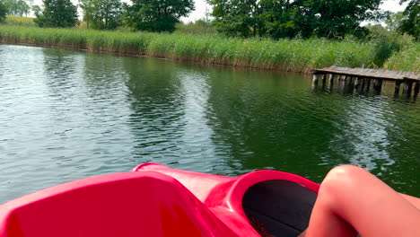 Woman-rides-water-bike-close-to-shore-with-wooden-platform-and-green-reeds