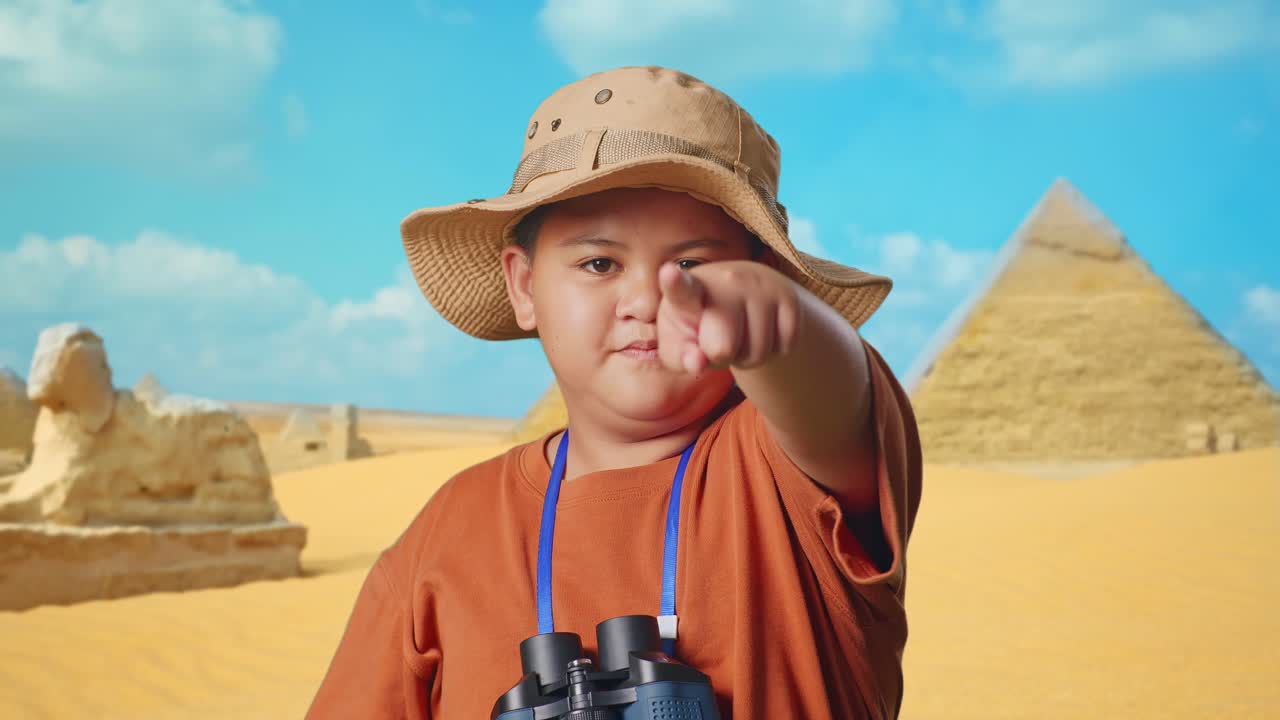 Asian Boy With Hat And Binoculars Using Magnifying Glass Pointing Finger Towards You, Shaking Head Waving Index Finger While Traveling In Giza Pyramid. Boy Researcher Showing No Gesture, Close Up