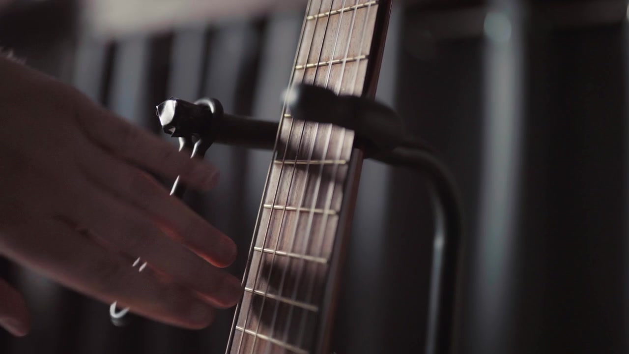 Hand stellt einen Kapodaster an einem Akustikgitarrenhals in einer schwach beleuchteten Innenumgebung mit weichem Fokus ein