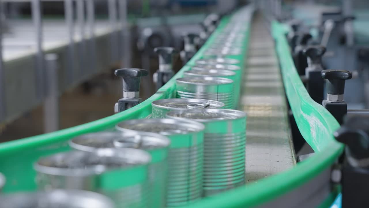 Cans moving on a conveyor belt in a food production line, featuring automation, packaging, sealing, and quality control in an industrial setting