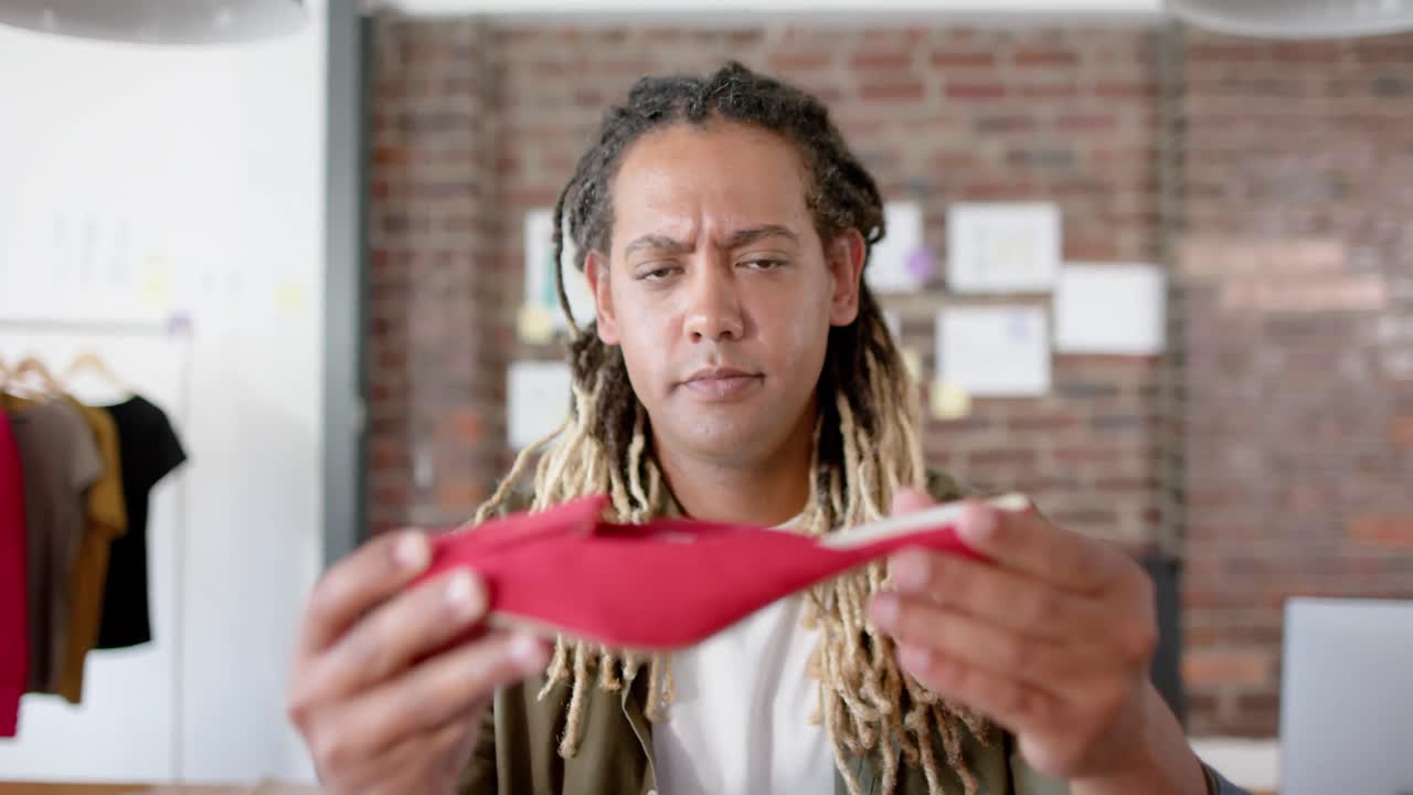 ritratto di un designer maschile bi-razziale felice che ispeziona una scarpa in uno studio di design di moda, in rallentatore.