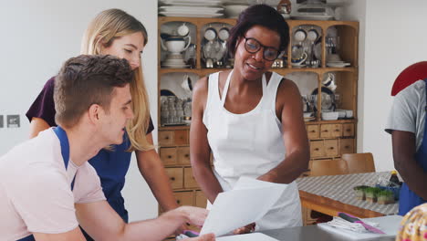 male and female adult students looking at recipe in cookery class in kitchen