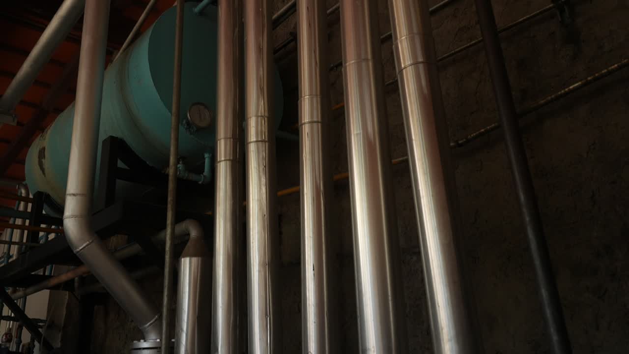Industrial destillation machine for tequila making. Metal tubes used for fluid transport inside a tequila distillery in Jalisco. Static upward-tilting closeup in 4K. Interior shot