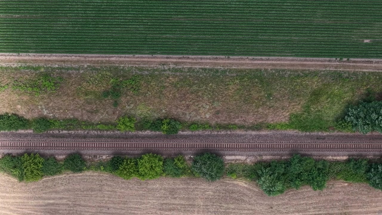 Una prospettiva aerea da drone mostra binari ferroviari paralleli che intersecano campi agricoli e vegetazione naturale