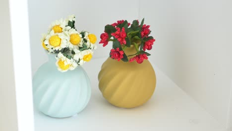 two vases with flowers on a white shelf