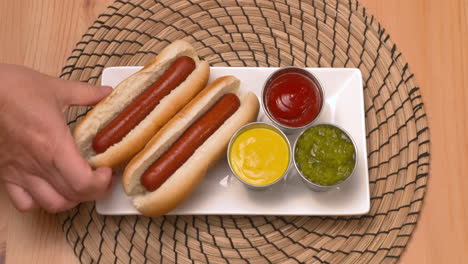 top down view of a hand removing hot dogs and condiments from a plate