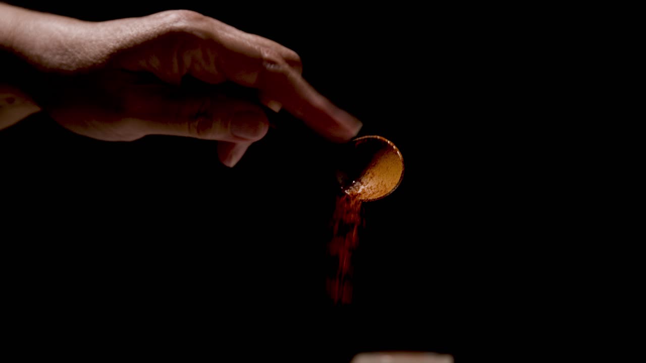 Paprika being sprinkled from a teaspoon on a black backdrop