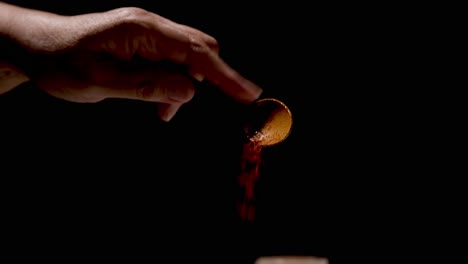 Paprika being sprinkled from a teaspoon on a black backdrop