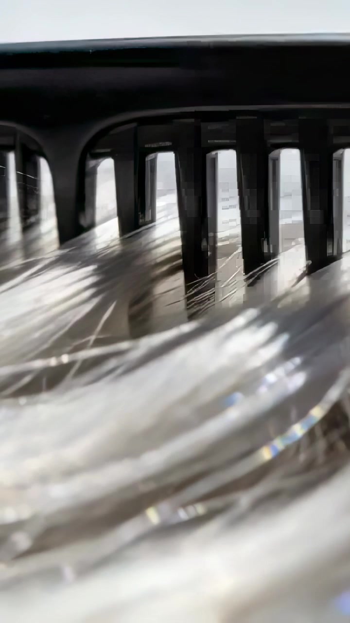 Vertikal video: Sort kam glider over lyse hårstrå på makrooverflade, viser glimtende fibre.