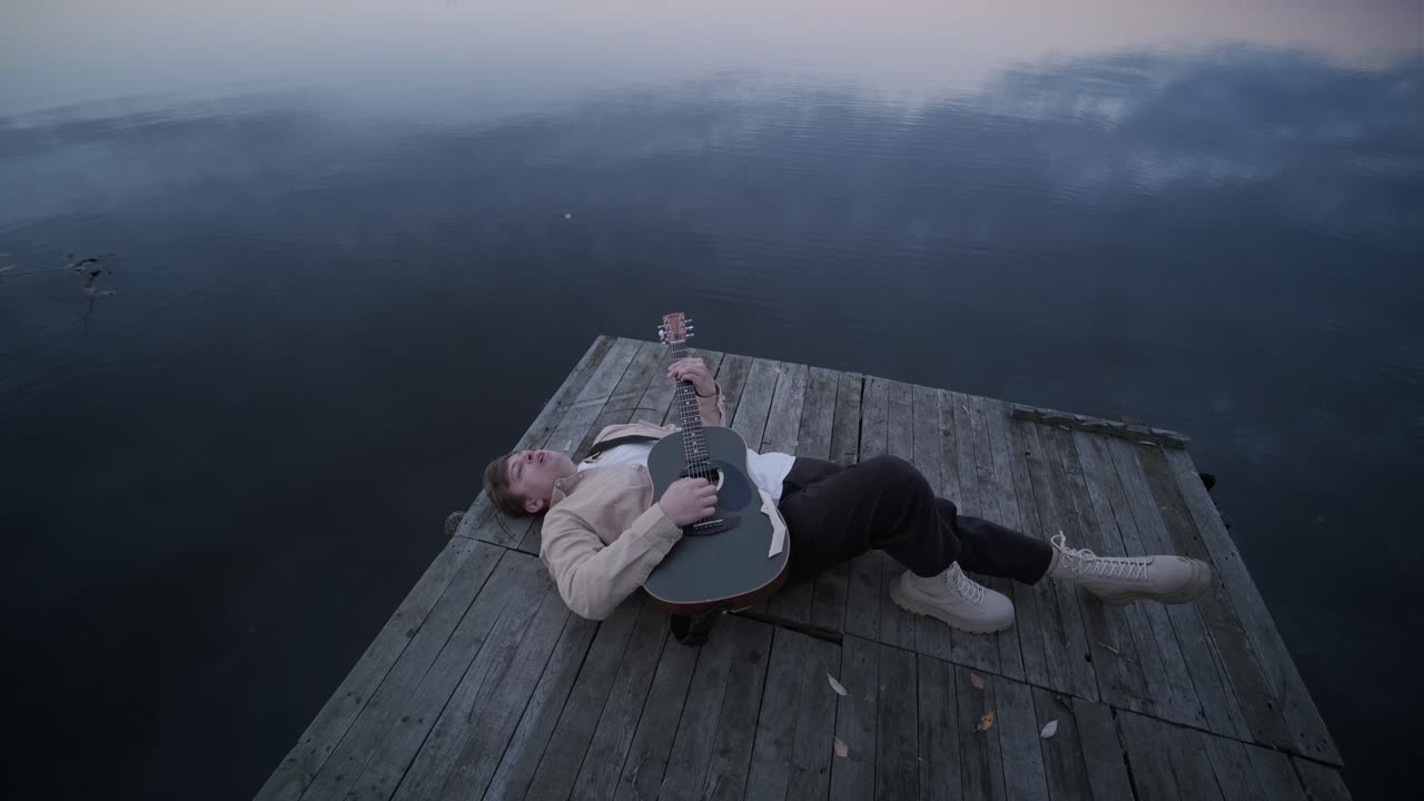 hombre tocando la guitarra en el muelle del lago