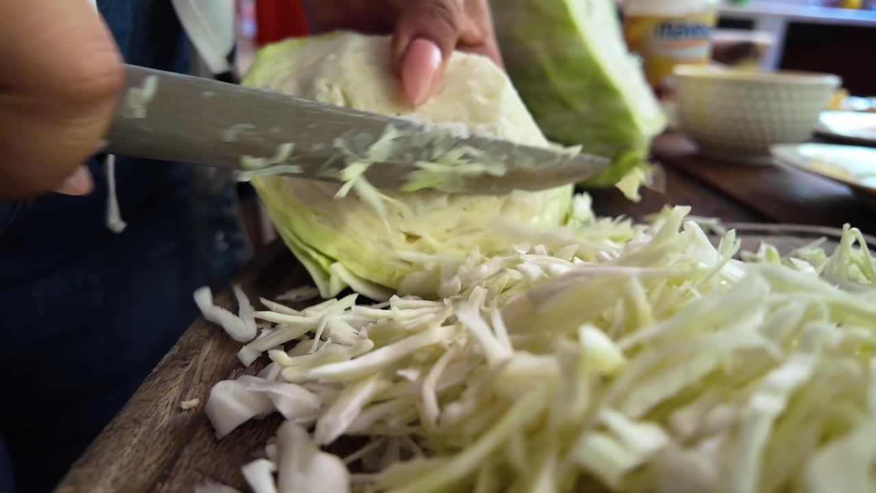 Plano real grabado cámara en mano que se centra en las manos de una persona y en un cuchillo preparando meticulosamente verduras frescas sobre una tabla rústica de madera