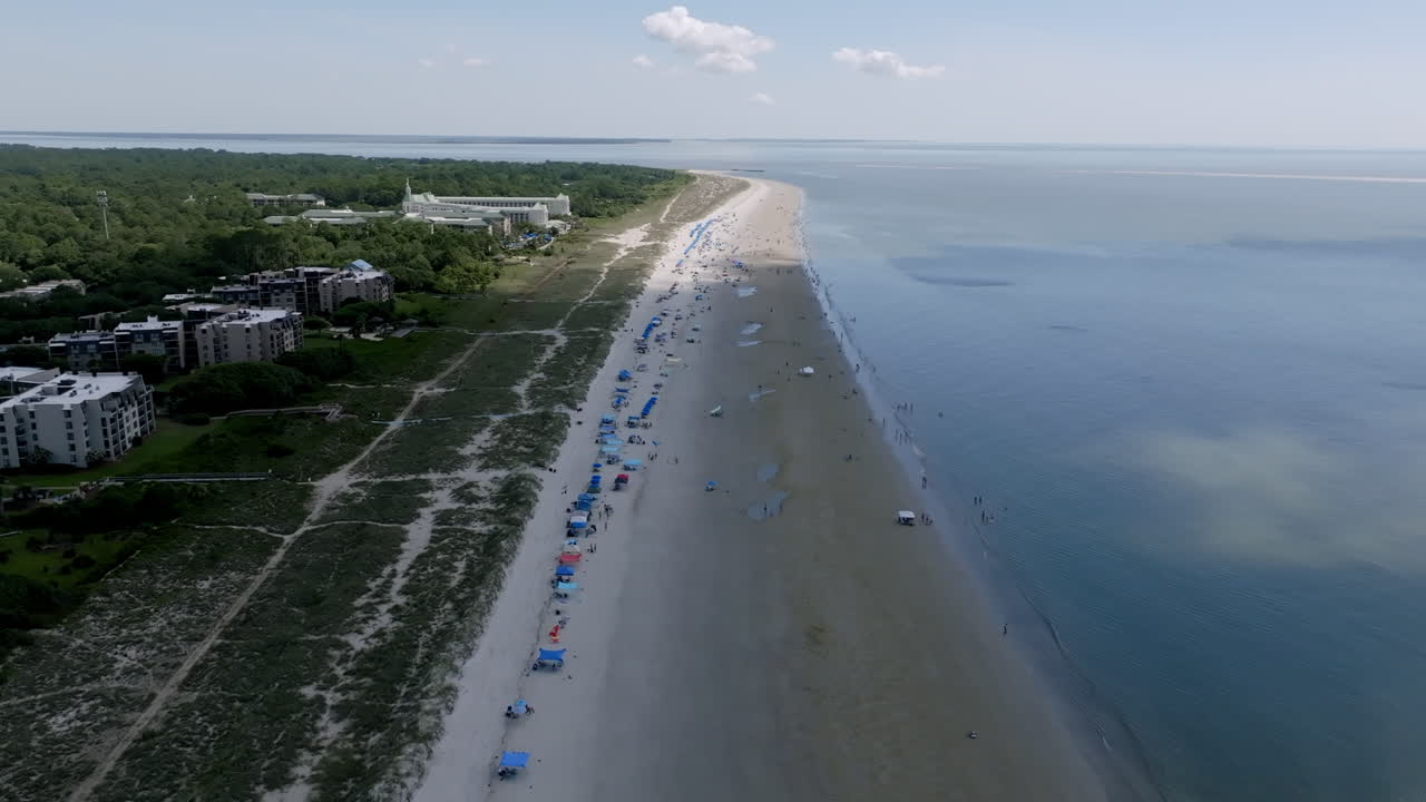 Drone shot of Hilton Head coastline with a long sandy beach stretching beside coastal resorts and calm ocean waters