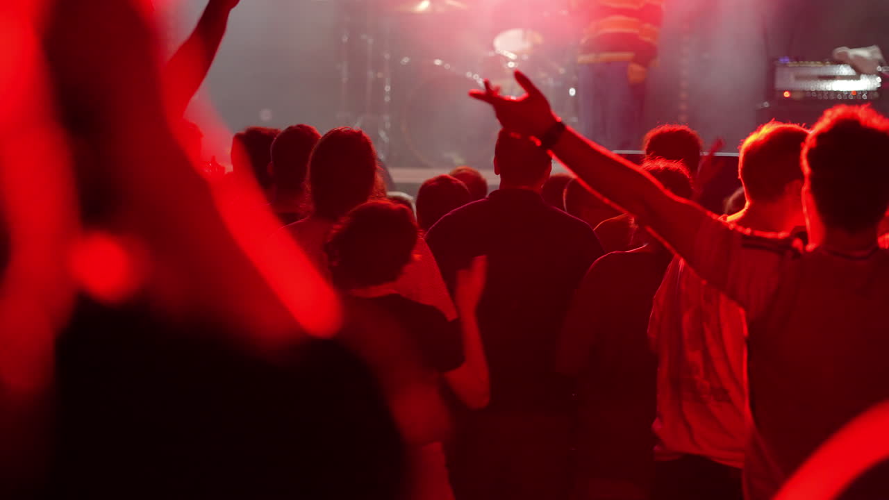 Crowd of enthusiastic concertgoers with raised hands enjoying live music performance in a dimly lit venue, creating an electrifying atmosphere of excitement and energy