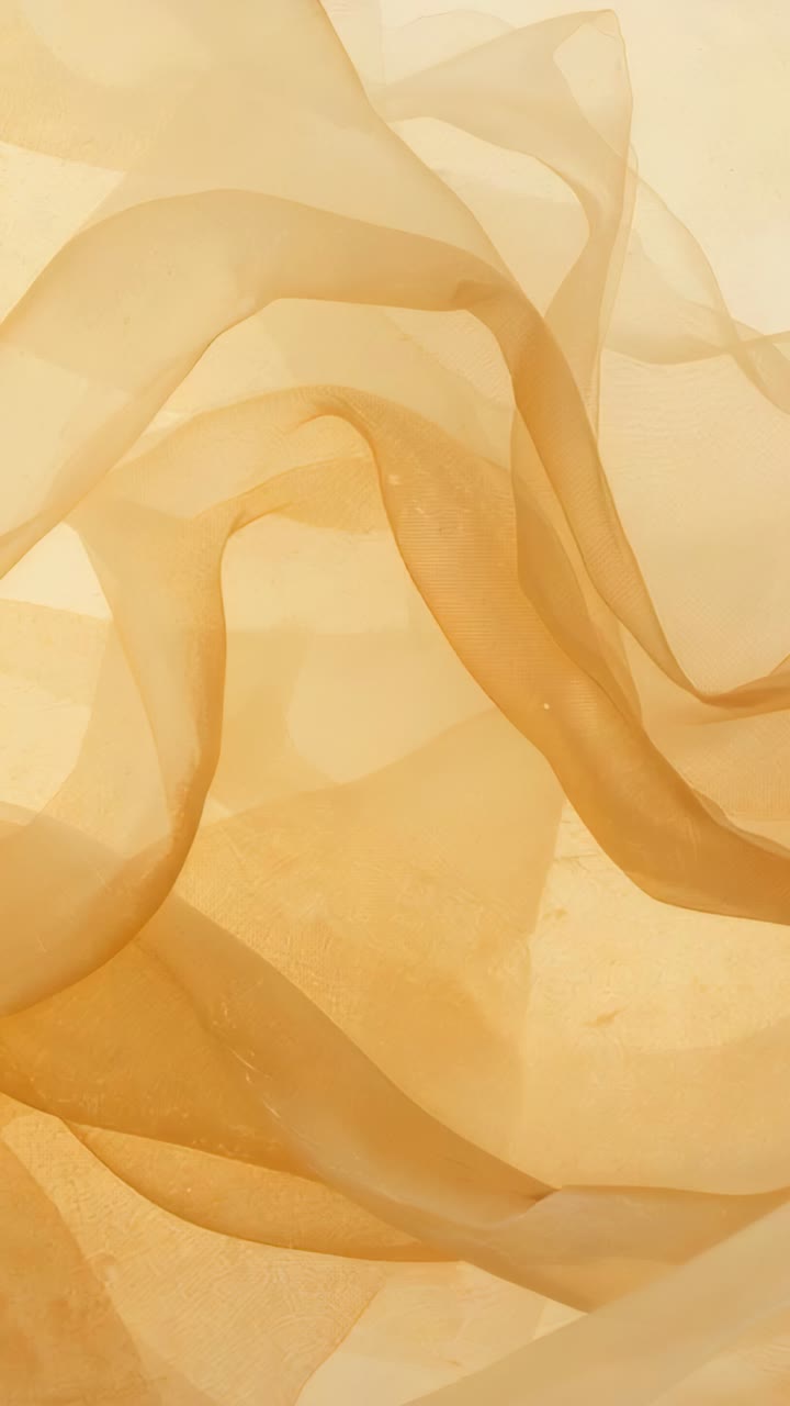 Vertical video: Shifting layers sheer beige cloth lifting right across frames in backlit studio