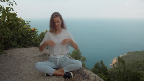 Girl doing yoga meditate on mountain peak with sea view on background