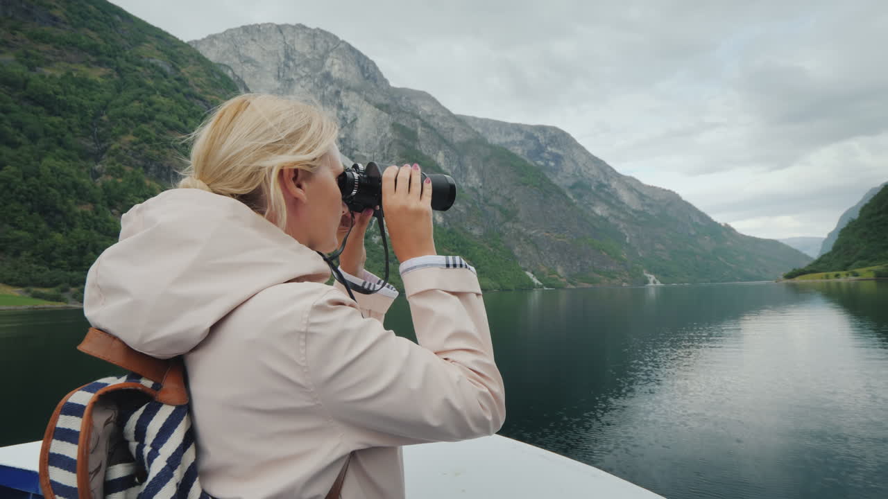 una mujer está de pie en la proa del barco mirando a través de binoculares crucero por los fiordos de noruega