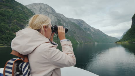 una mujer está de pie en la proa del barco mirando a través de binoculares crucero por los fiordos de noruega