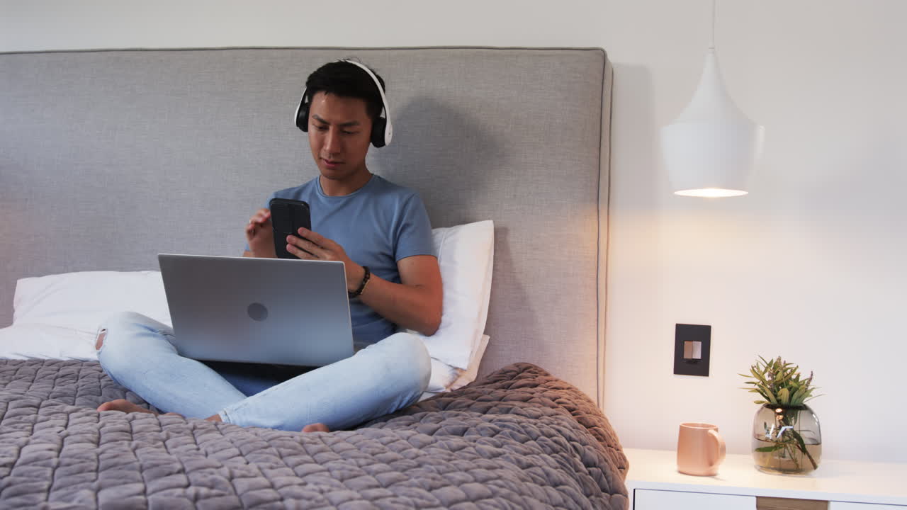 Relaxing at home, Asian man using smartphone and laptop, enjoying music