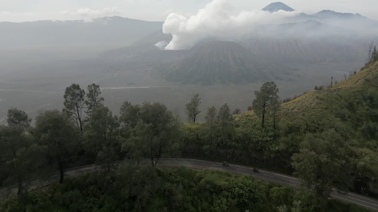 volcán en la distancia mientras las motocicletas viajan por una carretera de montaña torcida