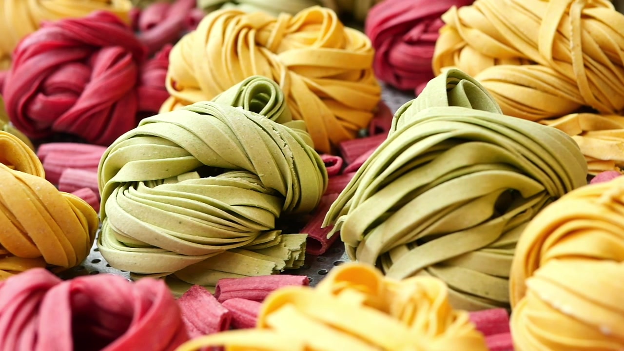 Nidi di pasta fresca colorata disposti su un vassoio di metallo