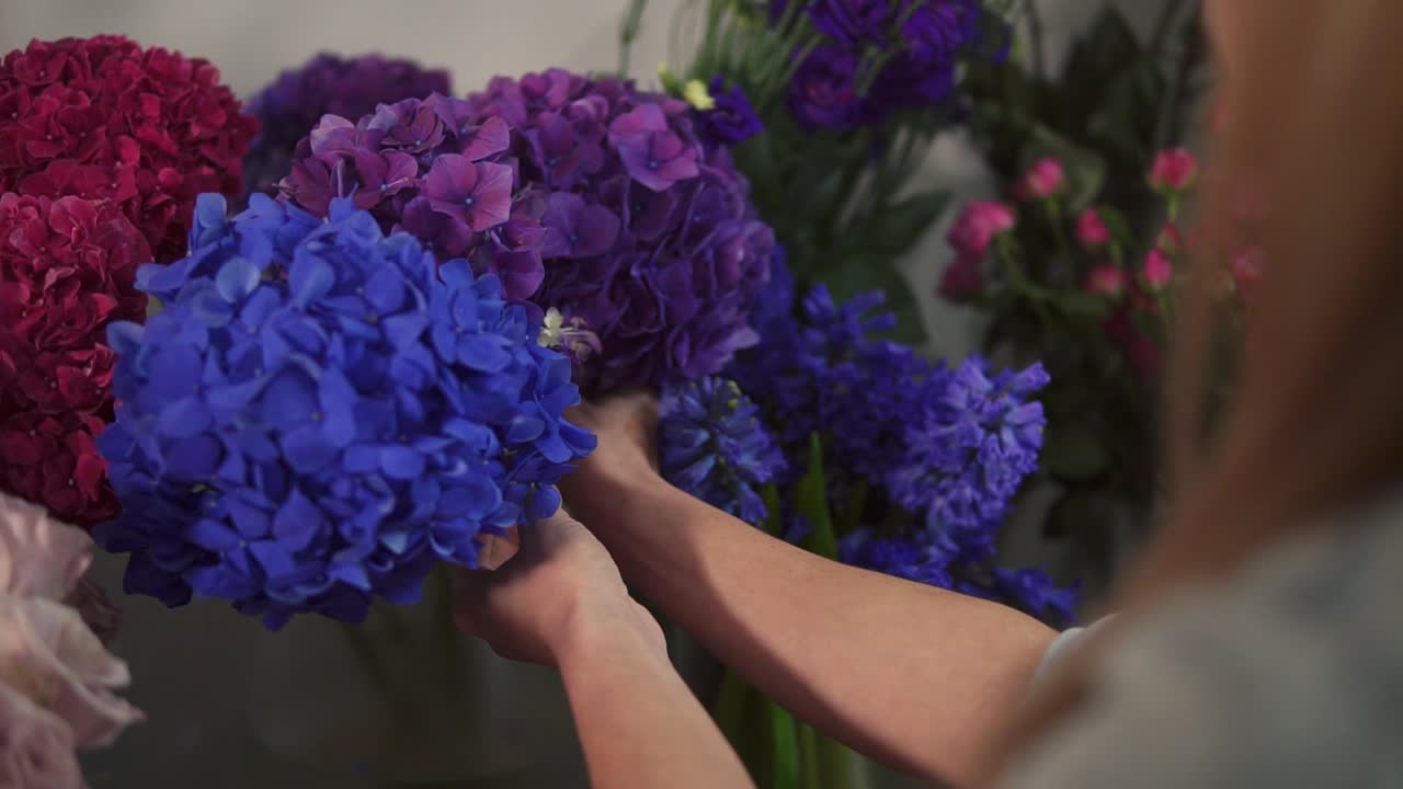 Back view of unrecognizable female florist business owner working and preparing flower arrangements in her shot, with fresh
