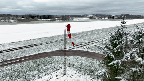 drone shot from a small snow-covered airfield, flying past the red and white windsock