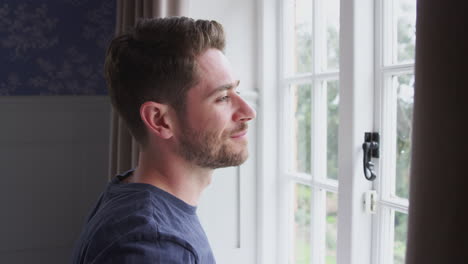 man wearing pajamas opening bedroom curtains at start of new day